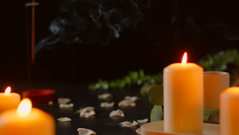 Still-Life-Of-Lit-Candles-With-Scattered-Flower-Petals-And-Incense-Stick-Against-Dark-Background-As-Part-Of-Relaxing-Spa-Day-Decor